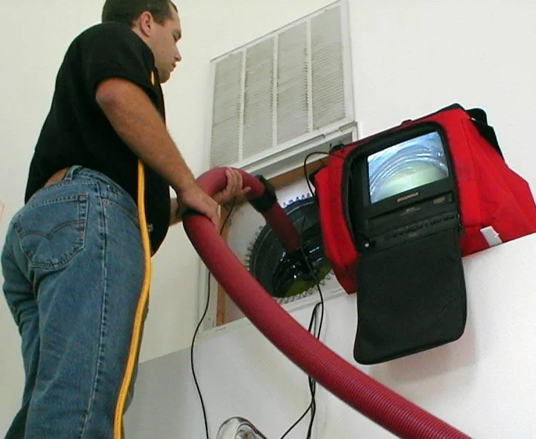 Technician using a duct cleaning and camera-monitor system at an AC opening
